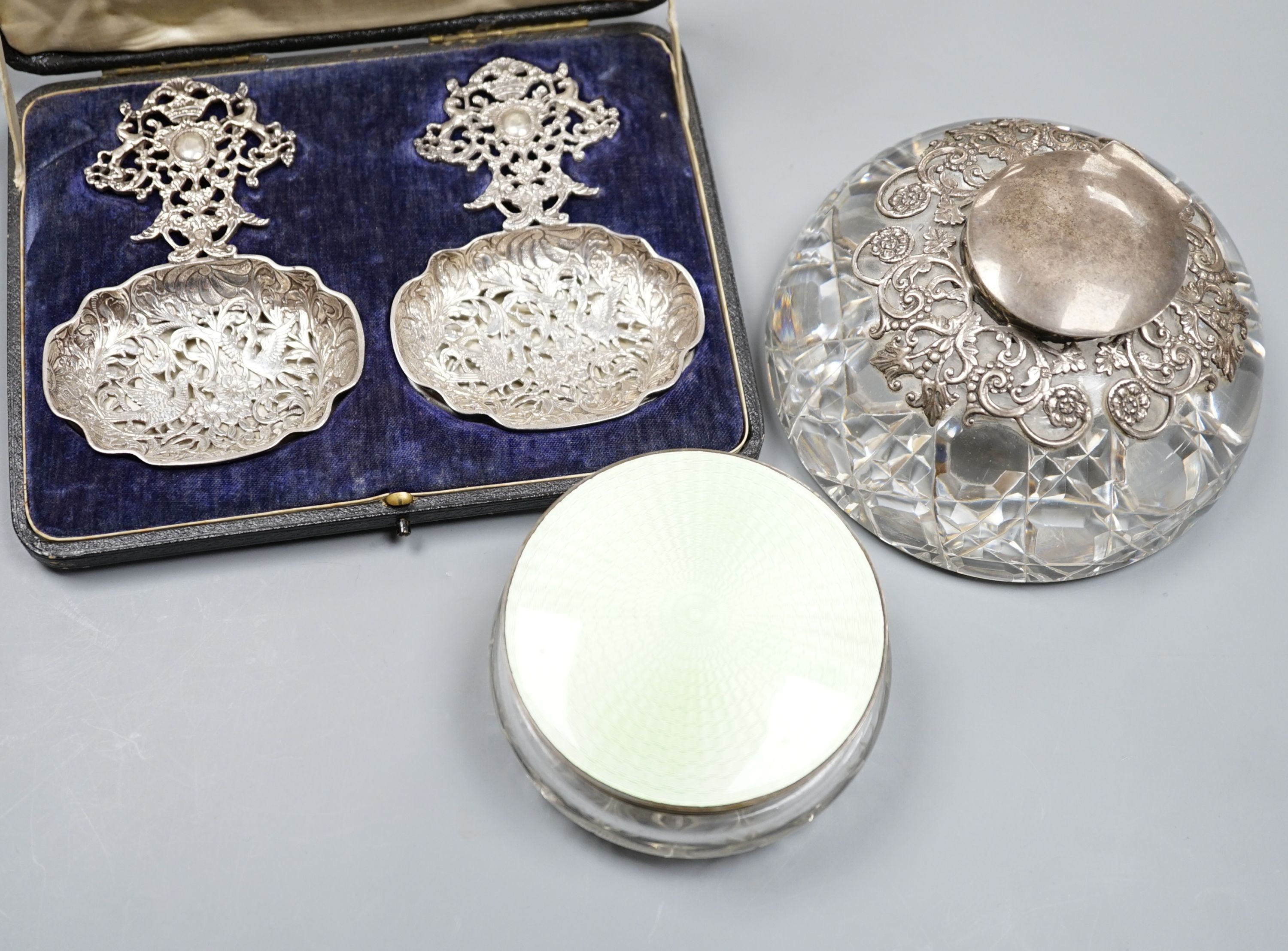 An Edwardian pierced silver mounted glass inkwell, London, 1901, 13.2cm, a silver and green guilloche enamel mounted glass powder jar and a cased pair of early 20th century ornate pierced silver spoons.